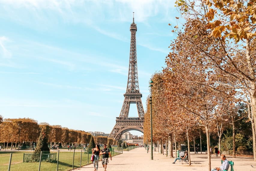 The Eiffel Tower stands in the background, with with grass of the Champ de Mars coming towards you, plus a wide unpaved walking path and trees. This is a popular arrondissement to stay in for first time visitors to Paris. 