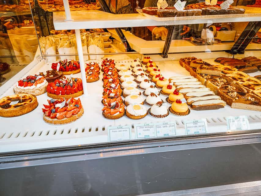 A pastry case in a boulangerie filled with fancy desserts, including eclairs, fruit tarts, flan, and lemon tarts. 