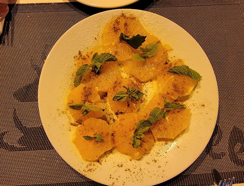 Orange slices are arranged on a plate and topped with cinnamon and mint leaves.