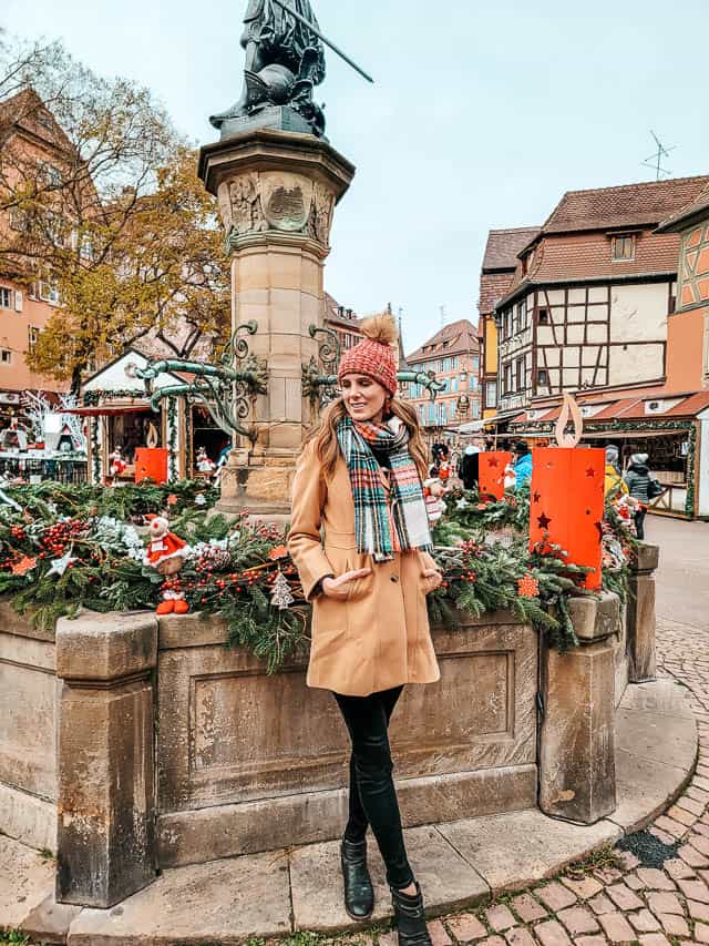 A woman stands near a decorated fountain in Colmar, France. This fountain, the Schwendi Fountain, was the model for Belle's town fountain in Beauty and the Beast.