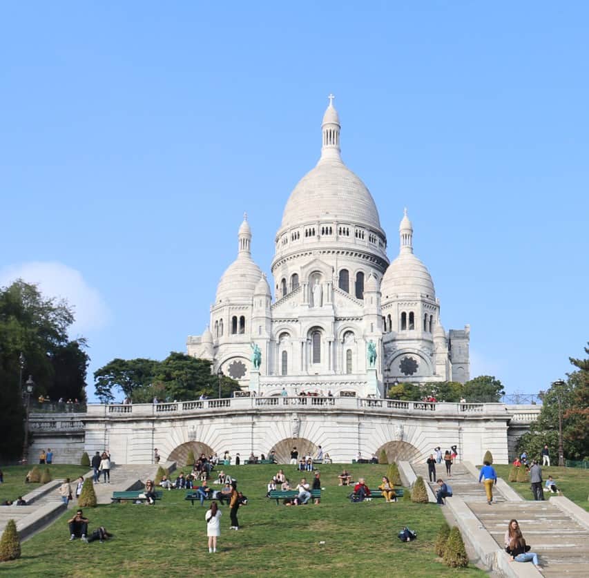The crisp white domes of Sacre Coeur church, with the staircases and lawn in front of it. 