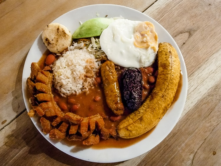 Bandeja Paisa. A plate of several traditional Colombian foods. Meat options such as pork rind, chorizo, and blood sausage. Plantain, rice, fried egg, and beans. 
