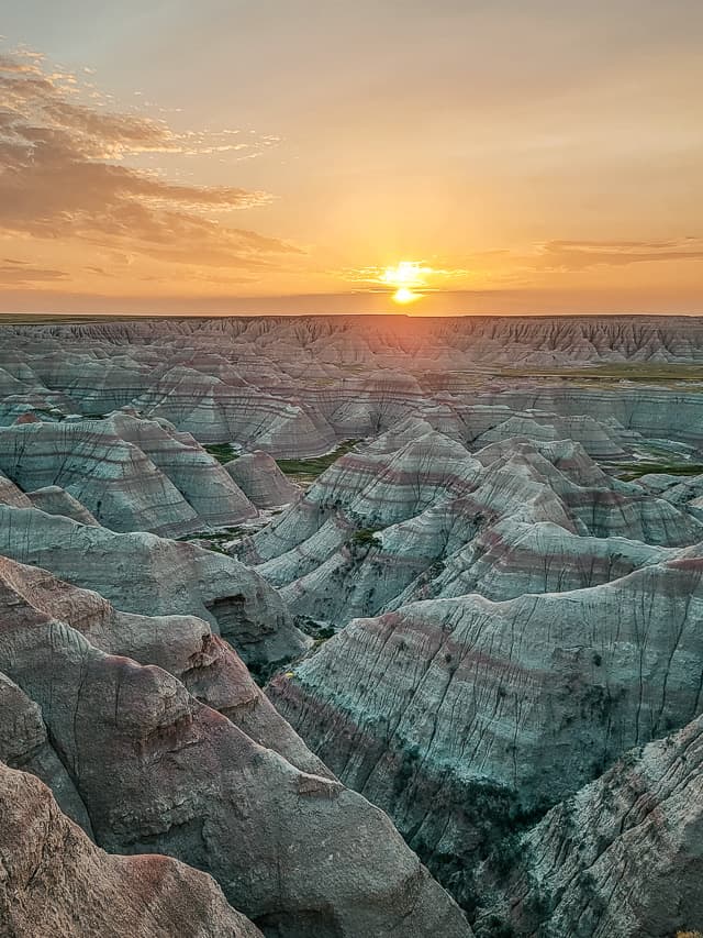 A beautiful sunrise over Badlands National Park. The sun rises over red and white striped rock formations.