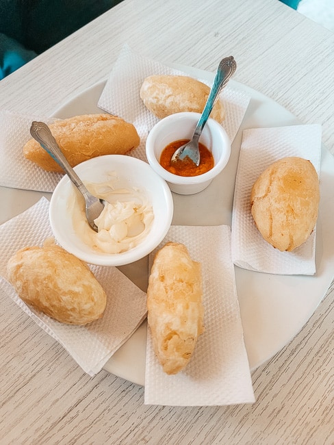 Five kasava and cheese treats on a plate with dipping sauces.