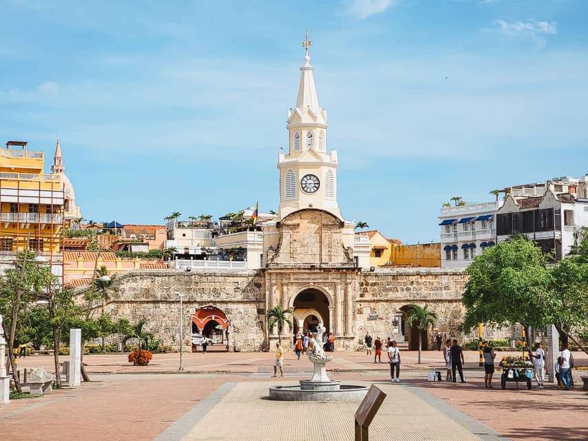 A town square with a stunning white steeple with a small fountain in the middle. 