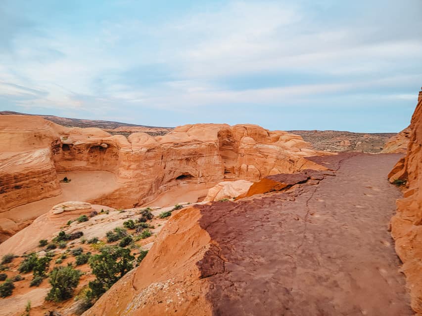 Rounded red ridges are seen from a ledge that makes the trail to Delicate Arch.