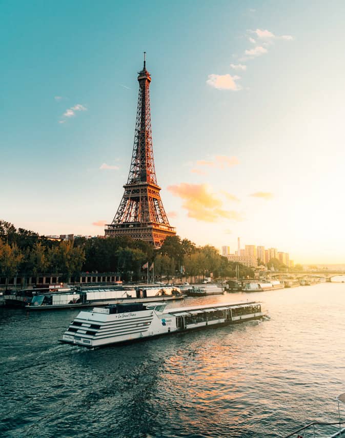 A riverboat glides in the Seine River past the Eiffel Tower just behind it. 