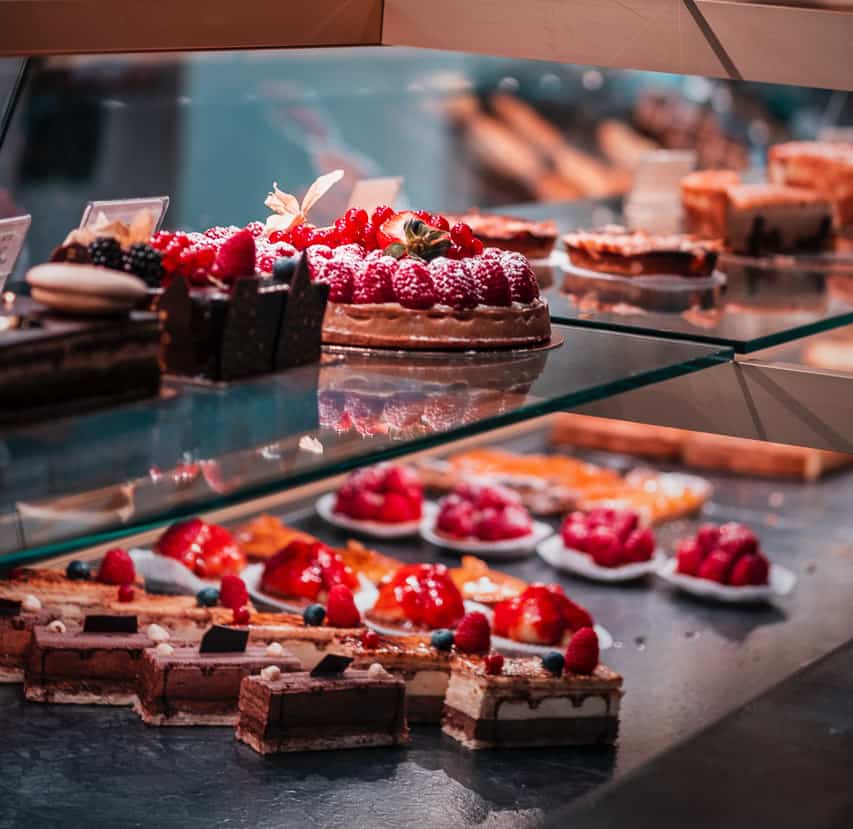 Multiple types of pastries made of chocoalate, raspberries, and strawberries fill a display case in a shop in a Parisian patisserie. 