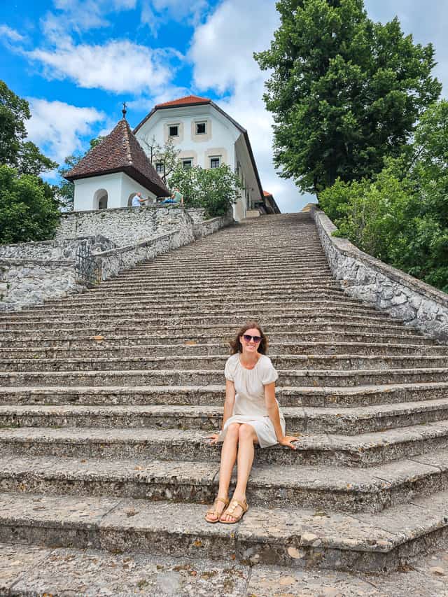 A woman sits on a 100 step large stone staircase on Bled Island.