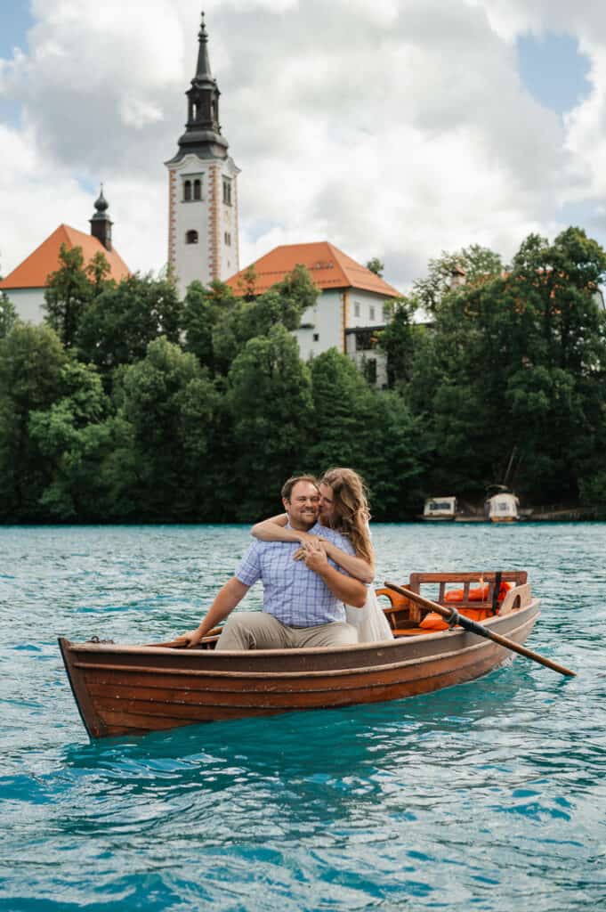 A man and woman wrap their arms around each other in a rowboat on lake bled, by the island. 
