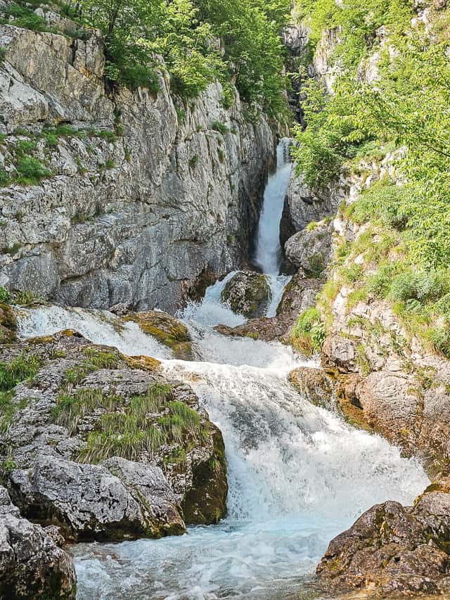 A waterfall sandwiched between rocks goes into a rushing powerful river. This is a unique slovenian waterfall. 