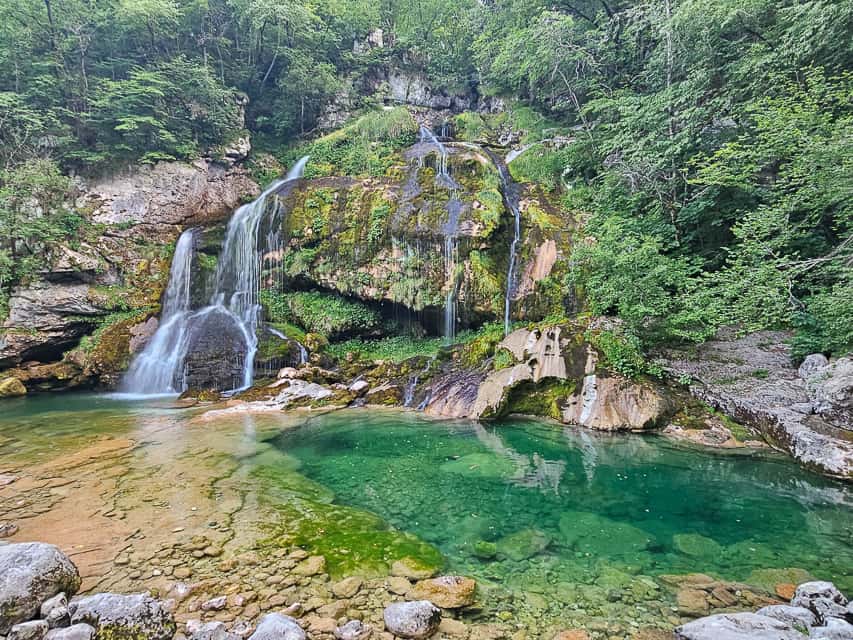 Multiple streams cascade down a rocky cliff, ending in a gorgeous deep turquoise pool - slap virje is one of the most beautiful waterfalls in slovenia. 