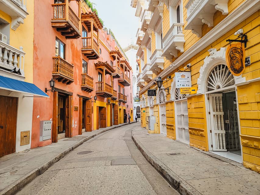 A very colorful and bright alley with yellow and pink buildings on a stone and cement street. 